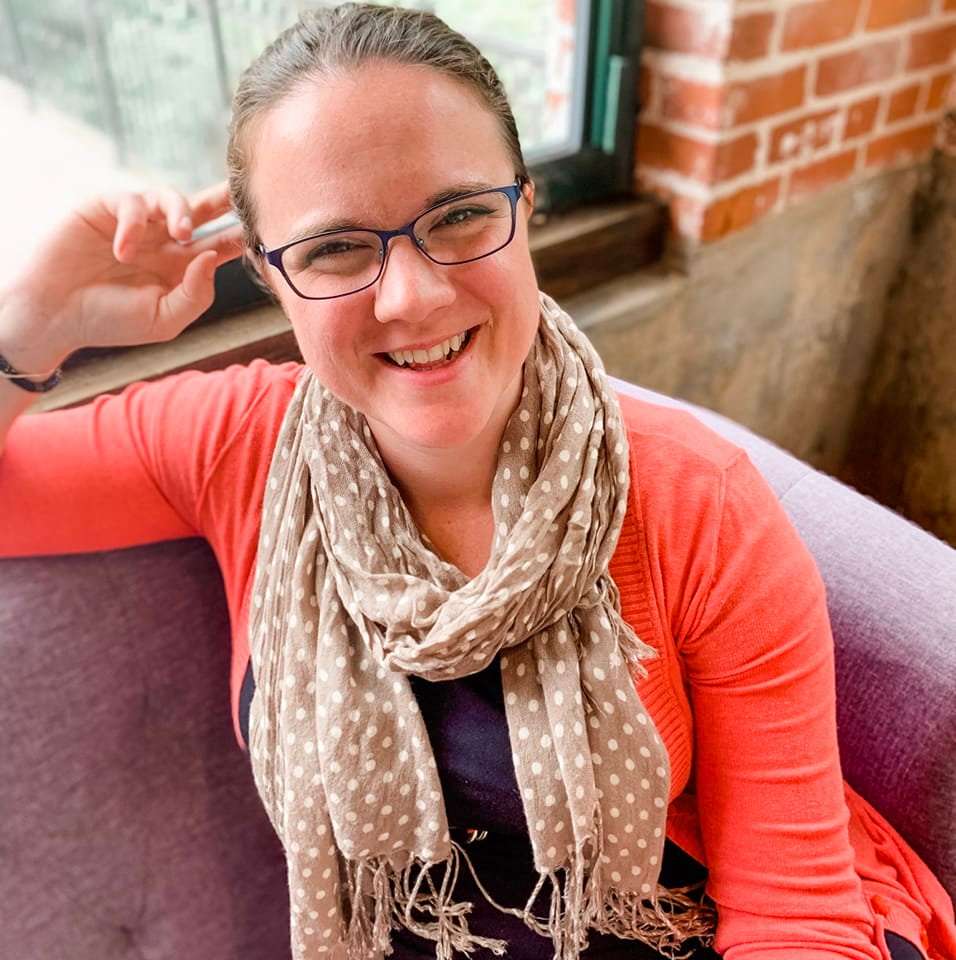 Meg Joyce, Inkind Brand and Design, Graphic Designer sitting on couch, smiling, orange sweater,